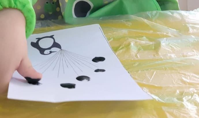 يد طفل تطبع بصمات سوداء على الورق أثناء نشاط الرسم في الحضانة